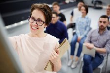 Femme souriante écrivant sur un tableau lors d'une formation, devant un groupe d'adultes attentifs
